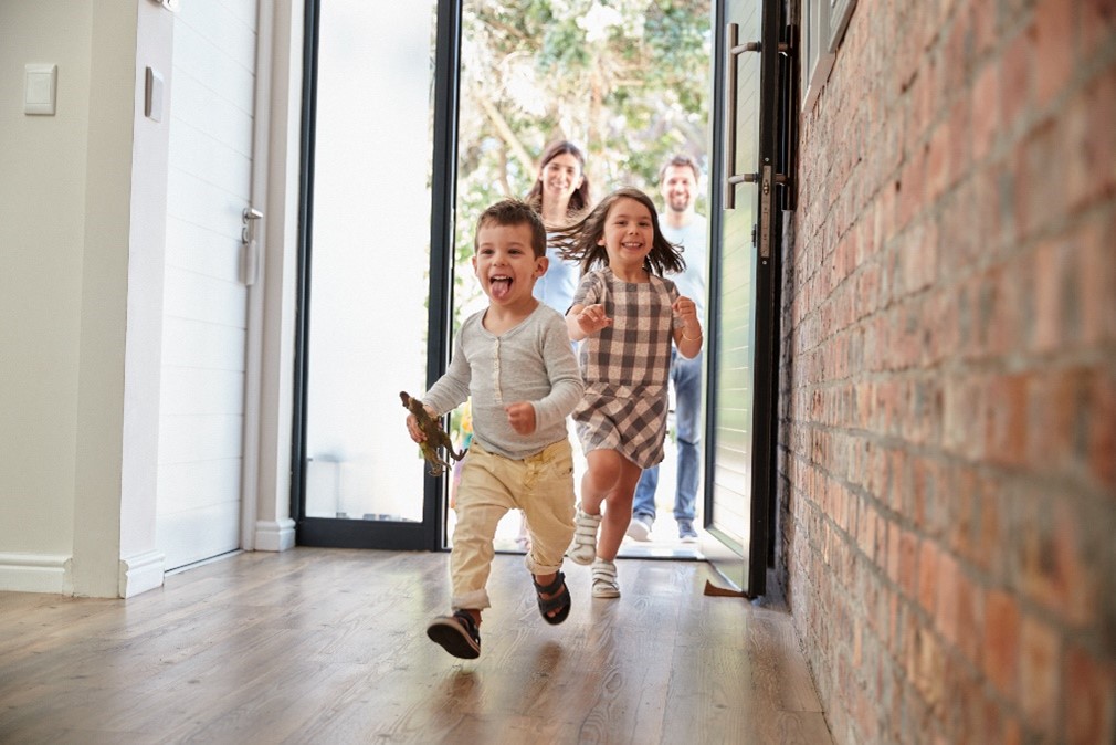 Children running inside of their home on vinyl flooring that resembles wood. 